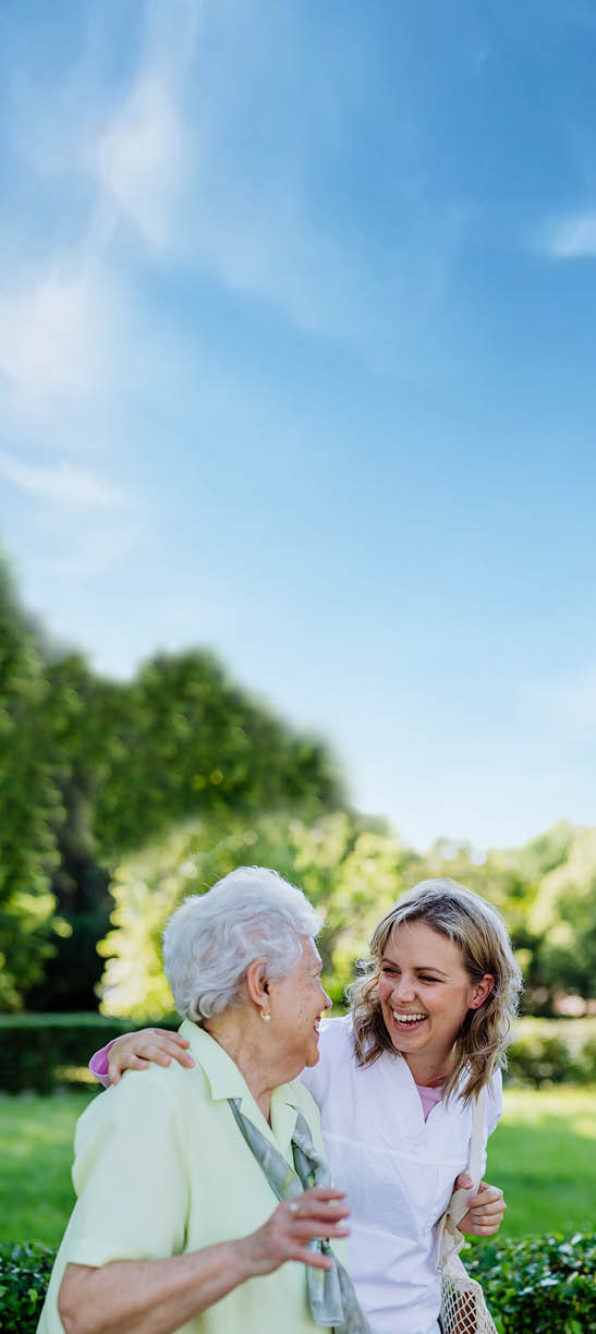 Portrait of caregiver with senior woman on walk in park.
