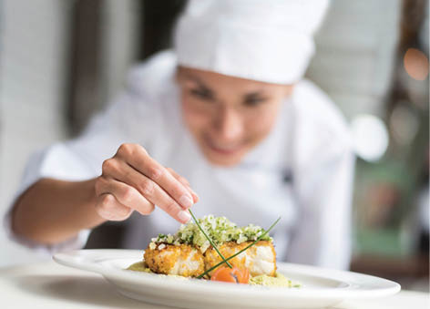 Cook decorating a plate and putting the ultimate touches - focus on foreground 